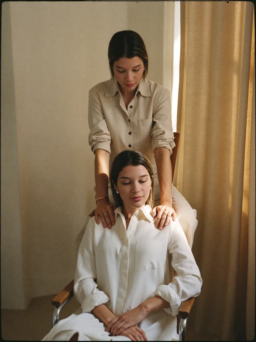 Vitoria aplicando Reiki, com as mãos sobre a cabeça de uma cliente deitada